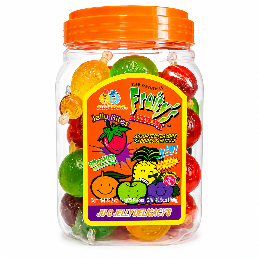 A clear plastic jar filled with assorted colorful jelly bites gummy candies, topped with a bright orange lid. The front features a large, colorful label for 'Juicy Misses' 'The Origin's Fruitiness Snacks'.
